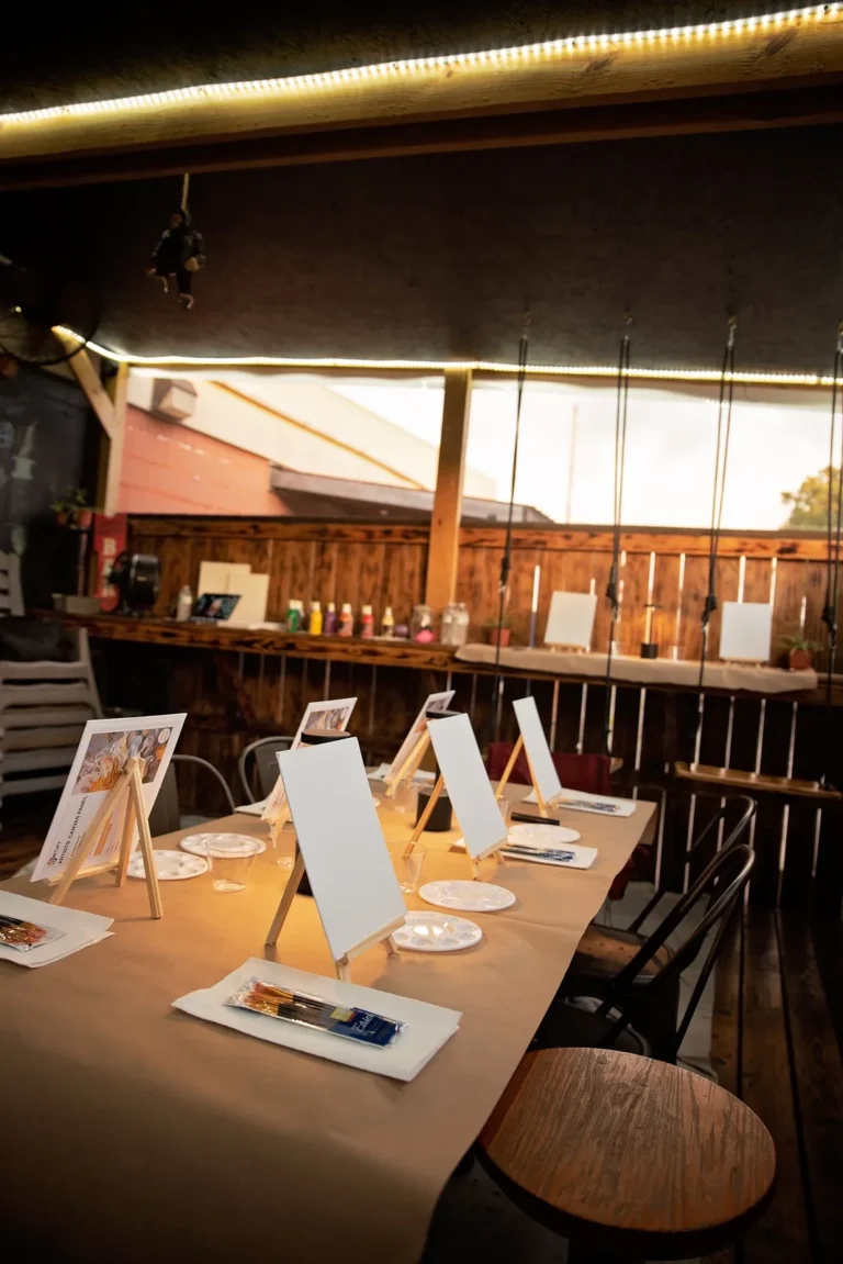 Outdoor patio tables arranged with canvases and painting supplies.
