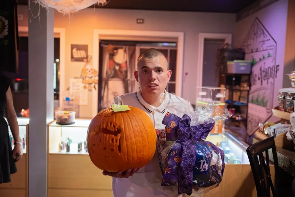 A guest poses with a carved pumpkin and Halloween prizes.